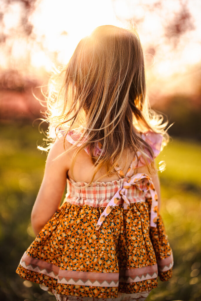 Family Photographer, a little girl stands in a grassy field at golden hour