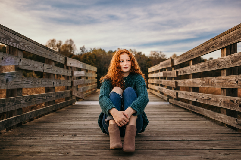 Family Photographer, a woman sits in the middle of a wooden foot bridge