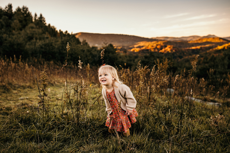Family Photographer, a young girls smiles as she stands in a grassy mountain meadow