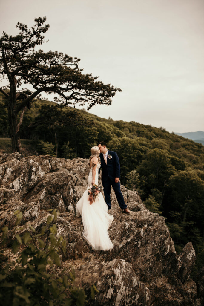 Wedding Photographer, bride and groom kiss standing atop mountain rocks